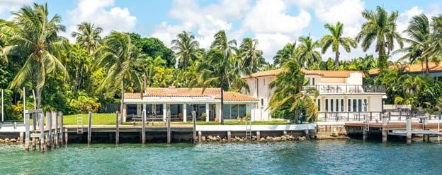 A luxurious resort in south india with a dock surrounded by palm trees. The resort is located on the shore of a body of water, and there is a boat docked next to it.